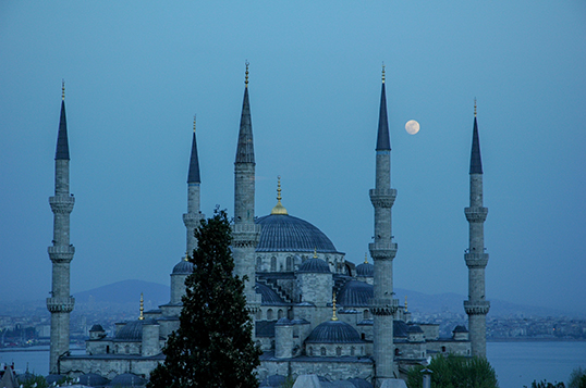 La mosquée Bleue à la nuit tombée à Istanbul en Turquie. La lune est présente au-dessus du bâtiment et l'ambiance bleue de la nuit ajoute une ambiance mystique à la photo.